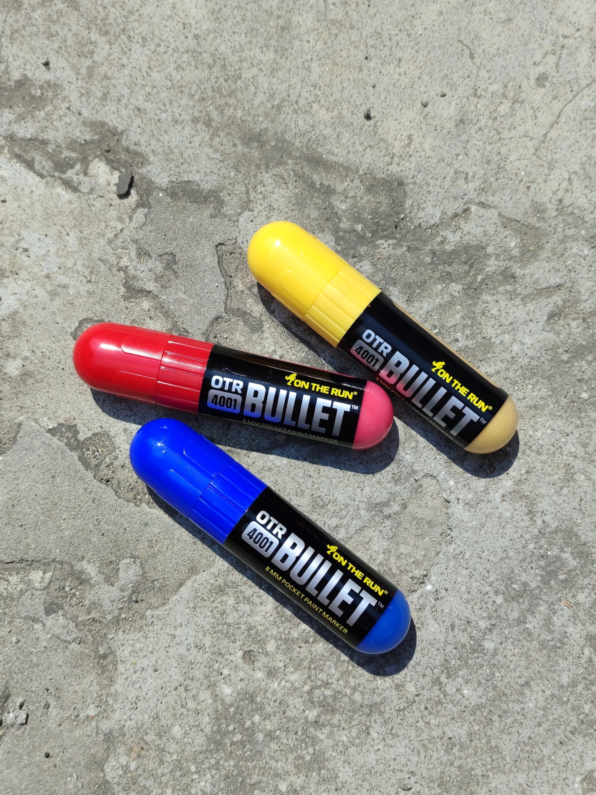 Three OTR Good Bullet markers in red, yellow, and blue on a concrete surface.