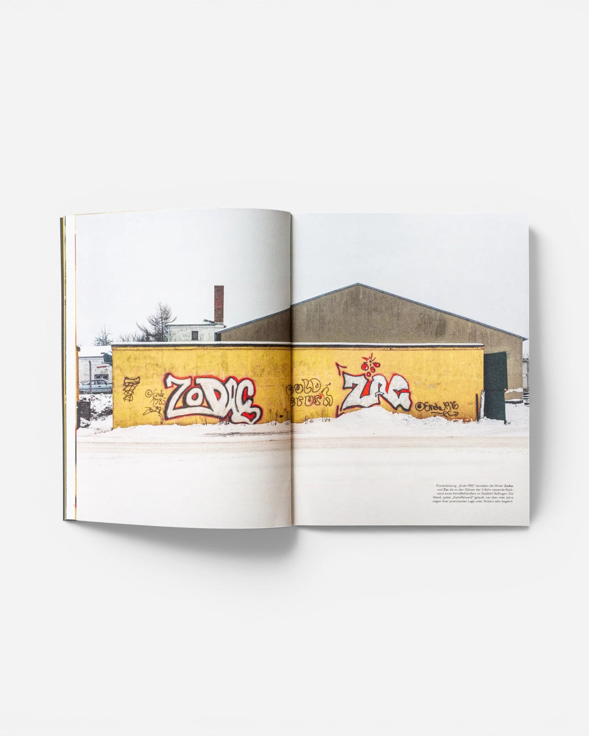 Open pages of Astrofat EINE STADT WIRD BUNT. – FLASHBACK book featuring 1985 graffiti on a yellow wall in winter.