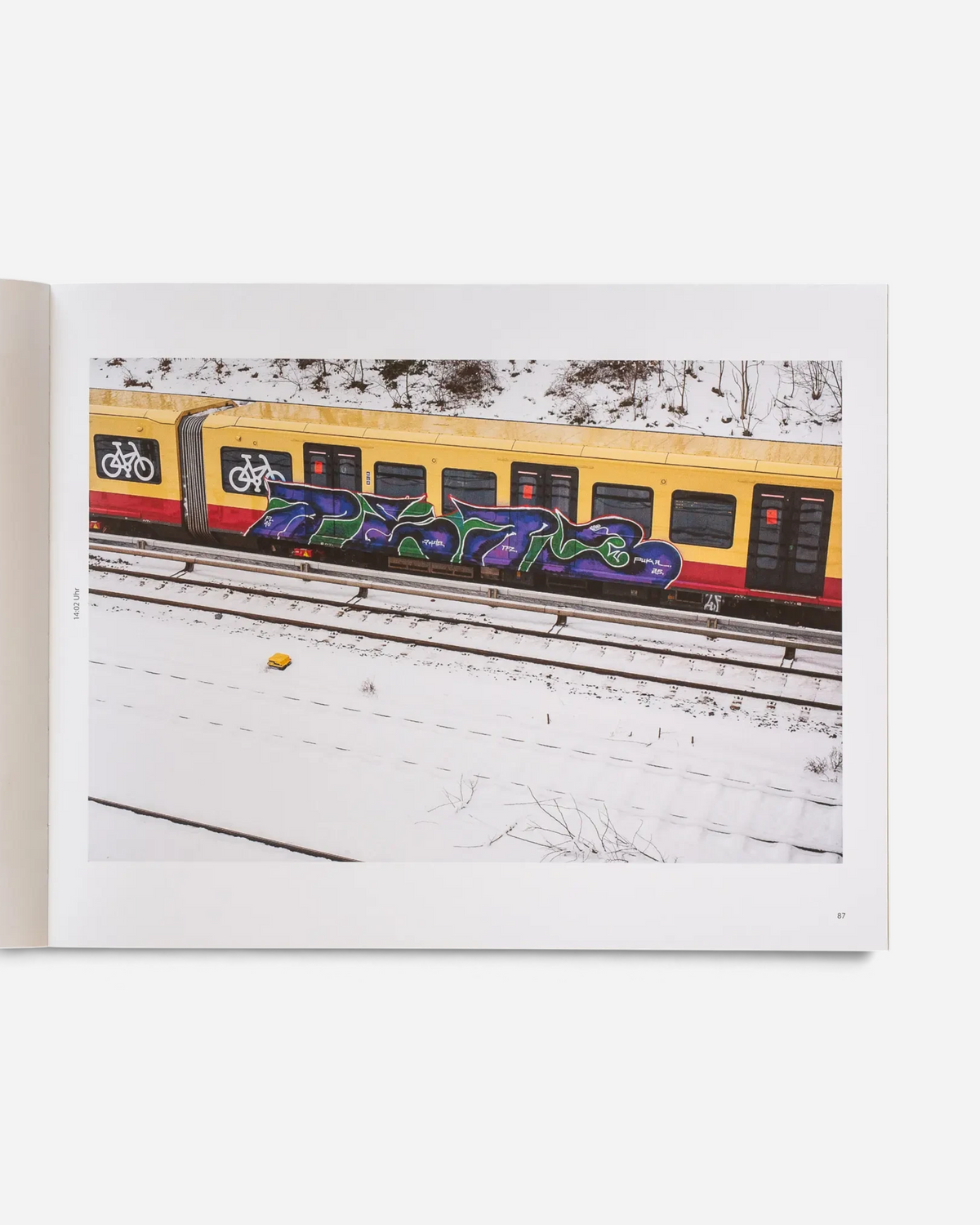 Astrofat Schriftzüge photobook open to a page showing a graffiti-covered yellow S-Bahn train in a snowy landscape.